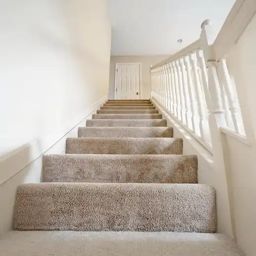 A carpeted staircase seen from the bottom looking up, with a handrail on the side.
