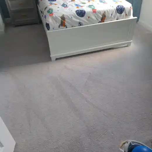 A high-angle view of a grey carpeted floor next to a chair with a decorative pillow.